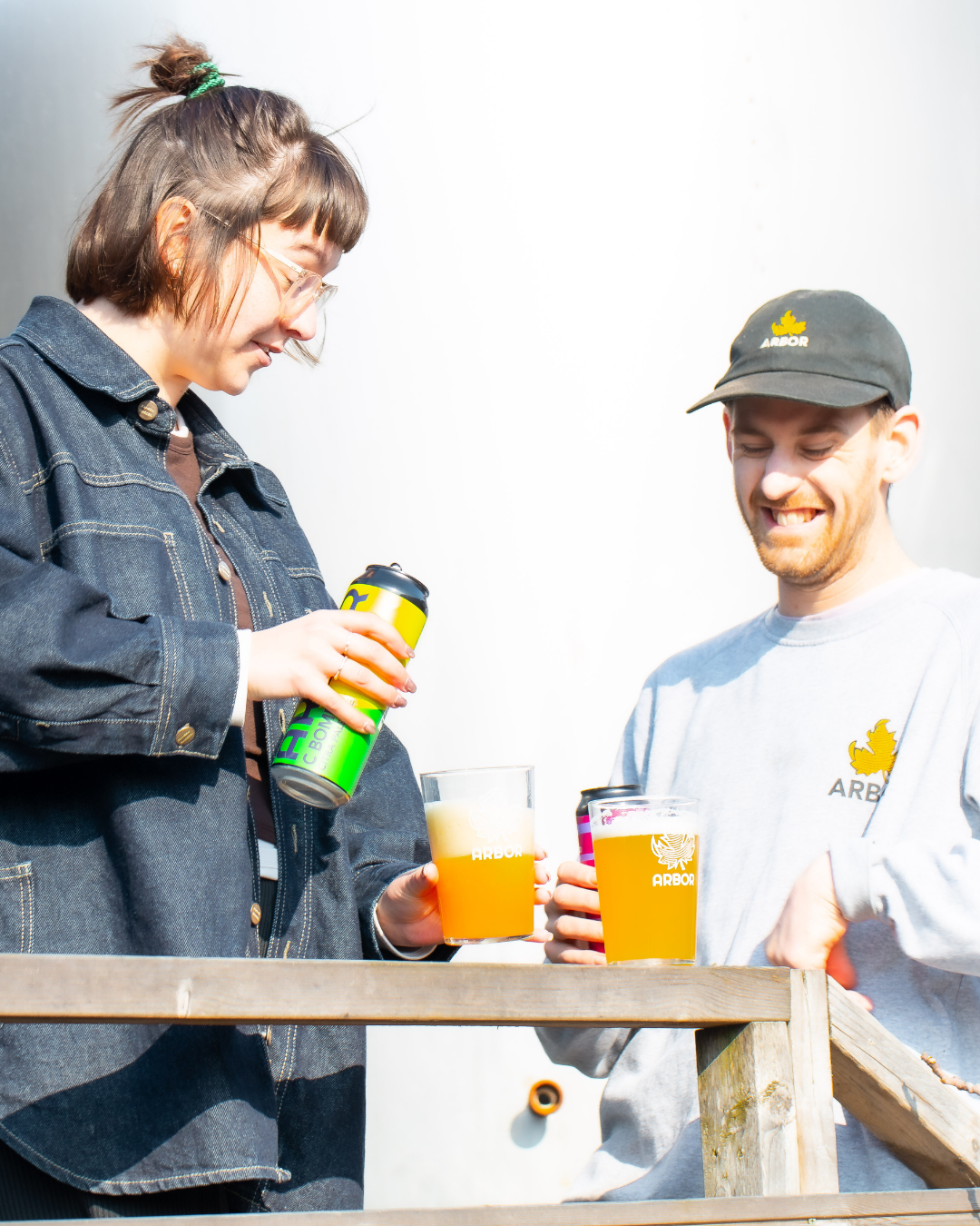 Two people enjoying drinks outdoors, one holding a can and the other a glass.