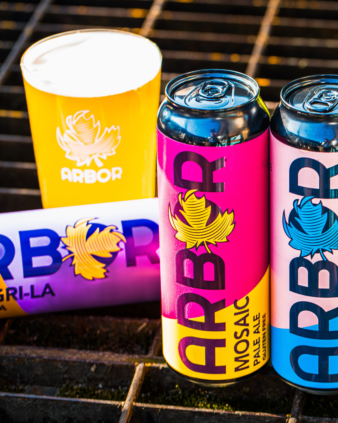Three Arbor Brewing cans on a grill with a yellow cup in the background
