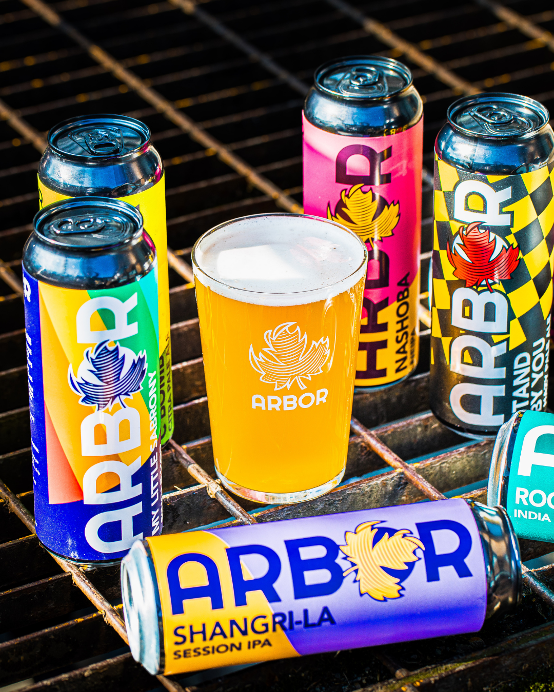 Assorted Arbor Brewing cans and a glass of beer on a metal surface