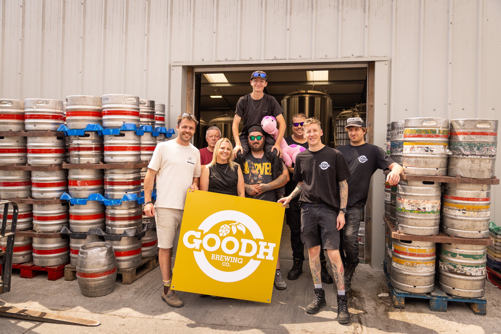 GOODH Brewing Co. team holding a brewery sign among beer kegs, a Brewser craft beer subscription partner brewery