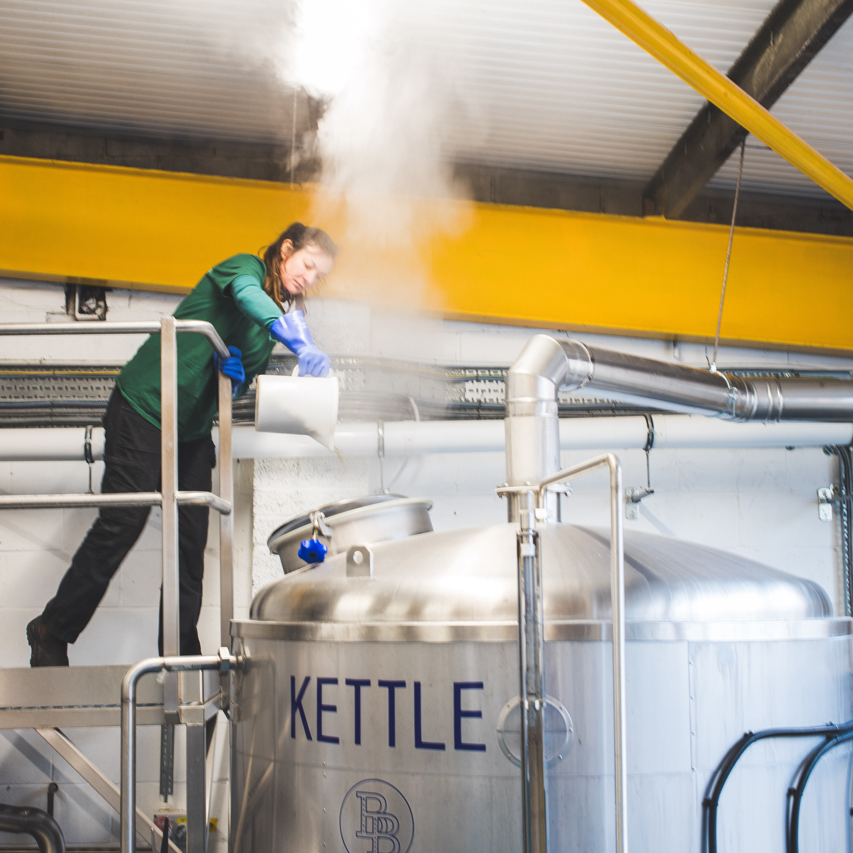 Brewer adding to the brew kettle at Brewing Brothers with steam rising, a Brewser craft beer subscription partner