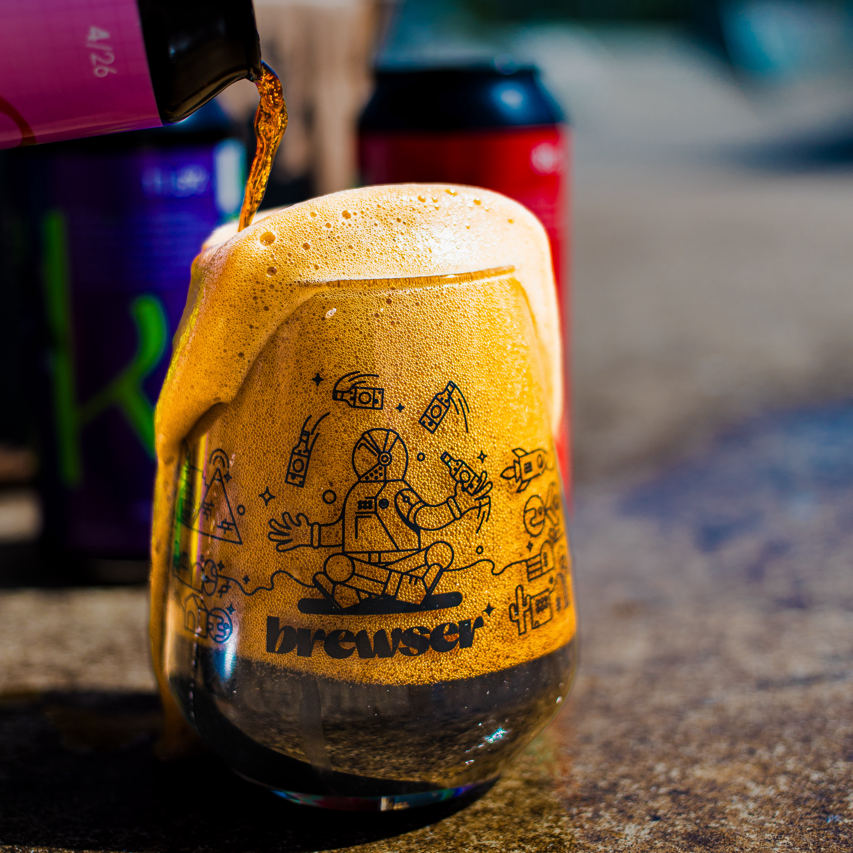 Brewser branded glass being poured with golden beer, Space Rat cans in background, craft beer subscription
