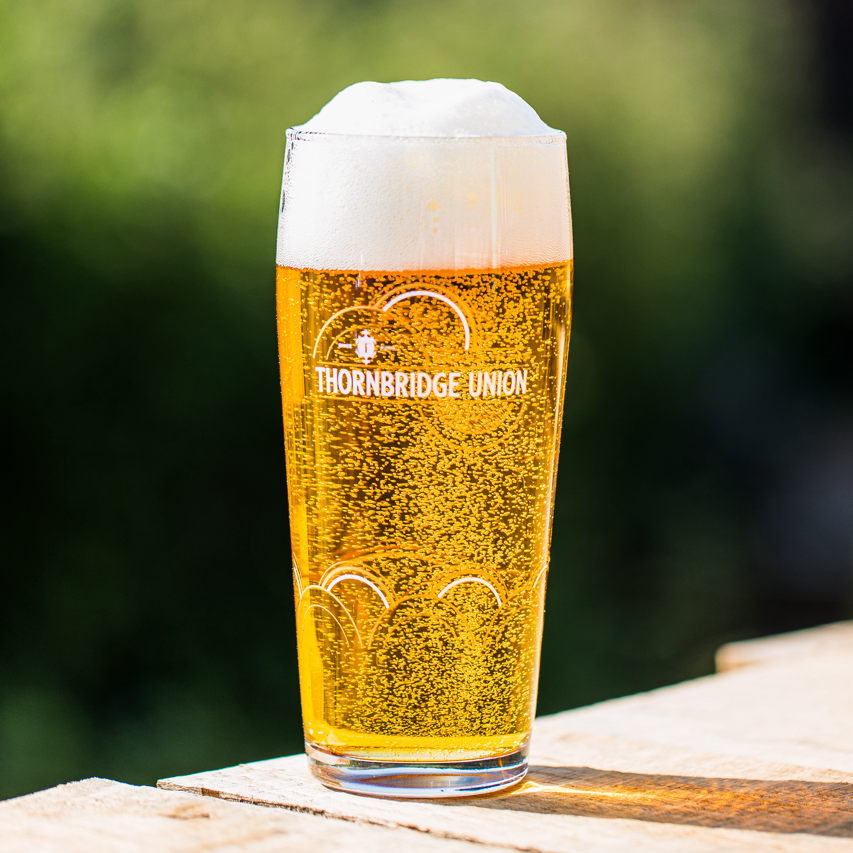 Pint of Thornbridge Union lager in a branded glass on wood outdoors, Brewser craft beer subscription