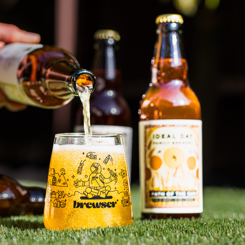 Ideal Day Family Brewery beer poured into a branded Brewser glass with bottles behind, craft beer subscription