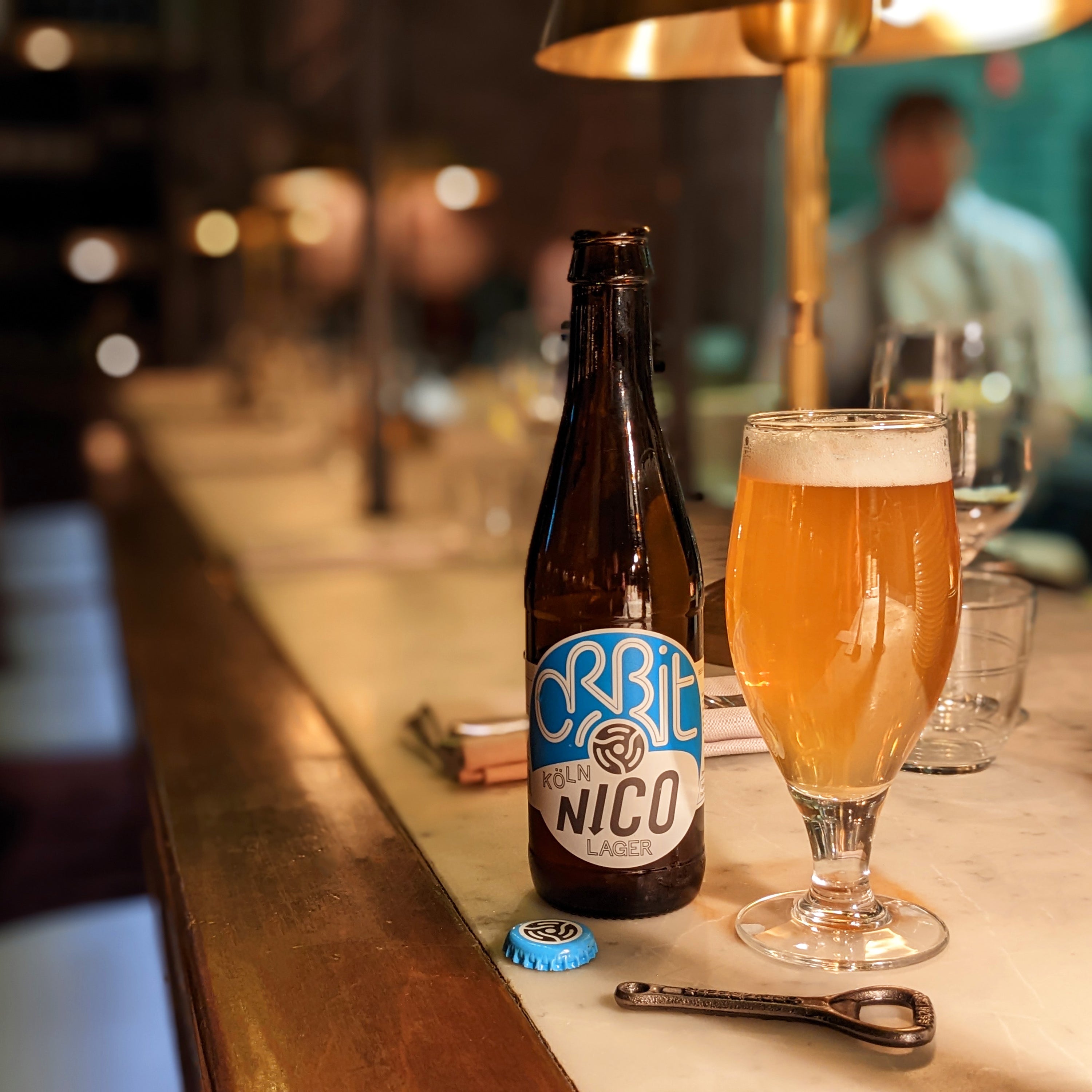 Orbit Beers Nico Koln Lager bottle and a poured pint on a bar counter, Brewser craft beer subscription