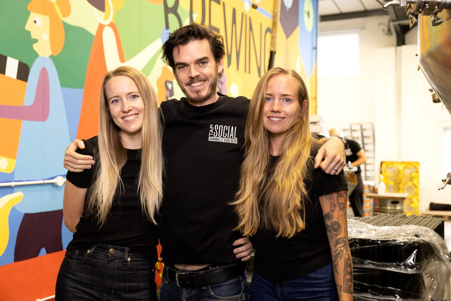 Tap Social Brewing founders in front of colourful brewery mural, featured in a Brewser craft beer subscription
