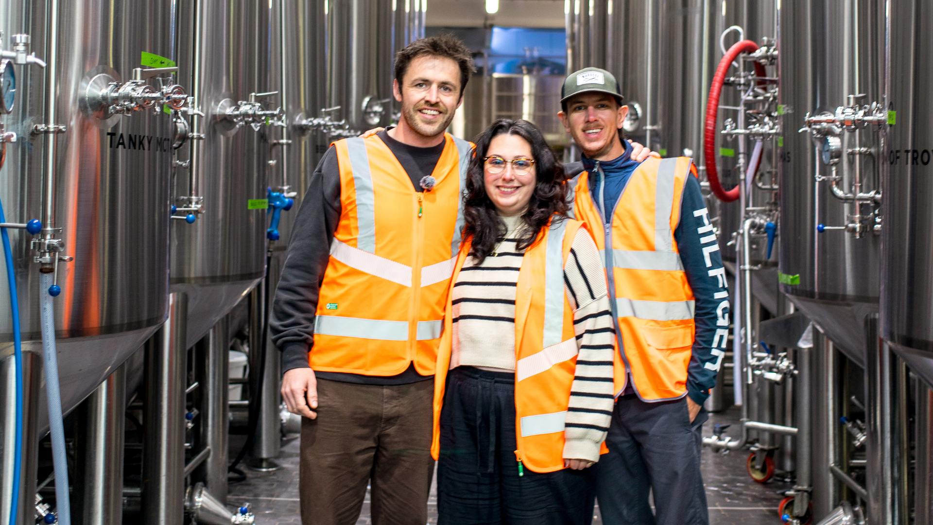 Brewser brewery visit with three people in hi-vis vests amid fermentation tanks, craft beer subscription brewery tour
